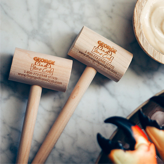 Image of George’s Wooden Mallet - Two wooden seafood mallets with handles, placed on a marble surface with a dish of stone crabs in the background.